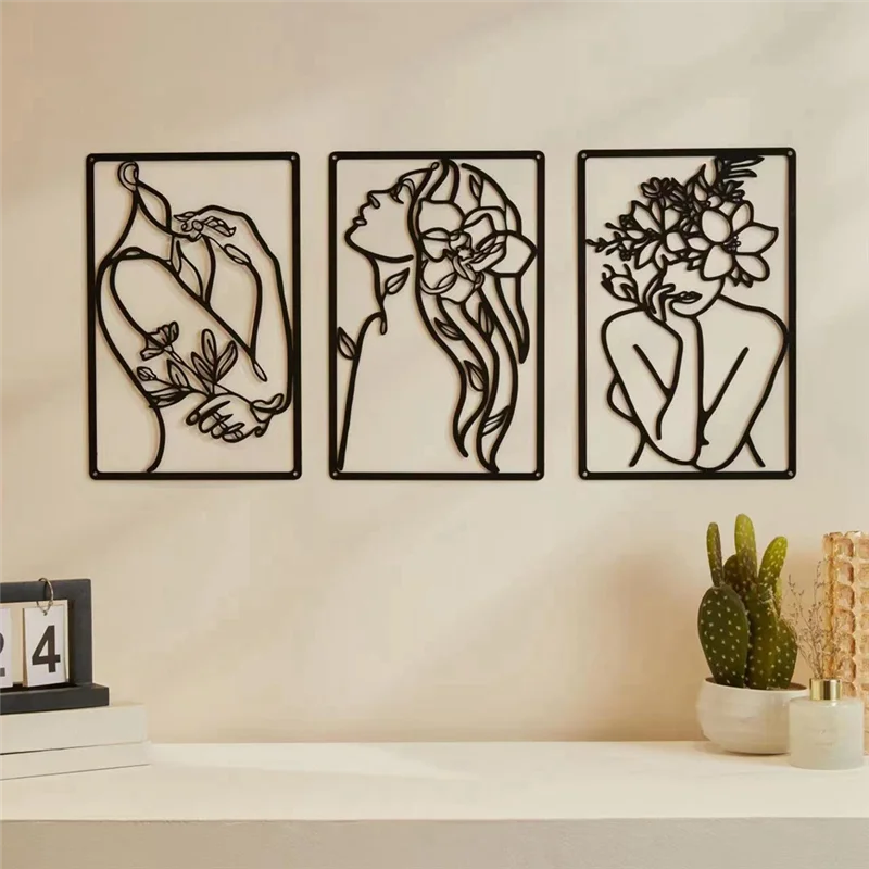 Three black metal wall art pieces on a beige wall with decorative items below.